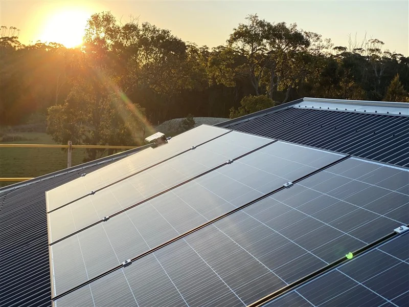 Rooftop solar array on a Colorbond roof at sunrise with sun flare over gum trees